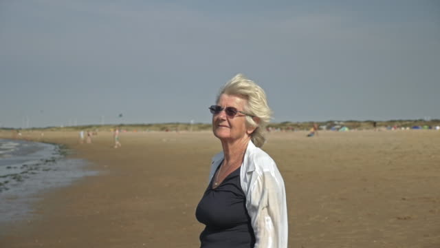 Ältere-Frau-stehen-am-Strand-Blick-verträumt-in-die-Ferne