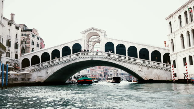 Ships-passing-under-amazing-Rialto-Bridge,-one-of-symbols-of-Venice,-Italy-and-ancient-heritage-of-world-architecture.