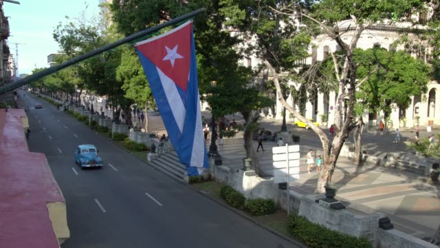 Yank-tank-classic-car-on-the-street-in-Havana-seen-from-above,-cuban-flag-in-La-Habana,-Cuba