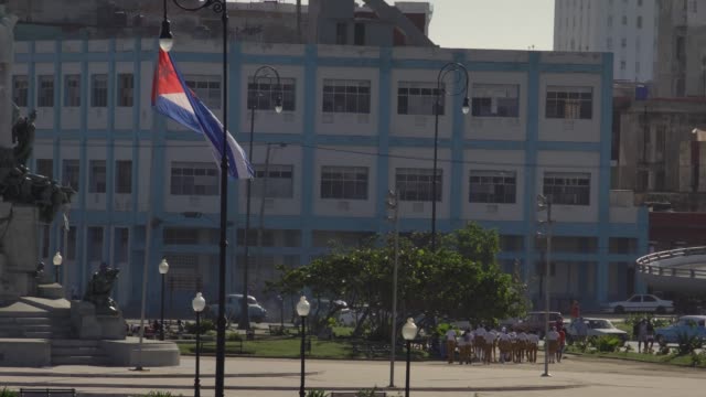vida-cotidiana-en-la-Habana-Vieja,-los-niños-de-la-escuela-cubana-en-plaza-pública-con-la-bandera-cubana