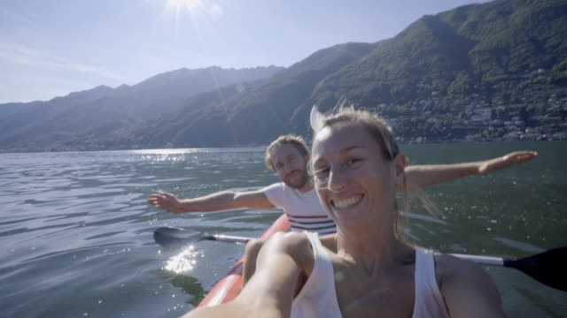 Young-couple-on-Summer-vacation-enjoying-canoe-on-the-lake-in-the-mountains.-People-travel-fun-holidays-concept.-Technology-and-youth-culture-taking-selfie---4K