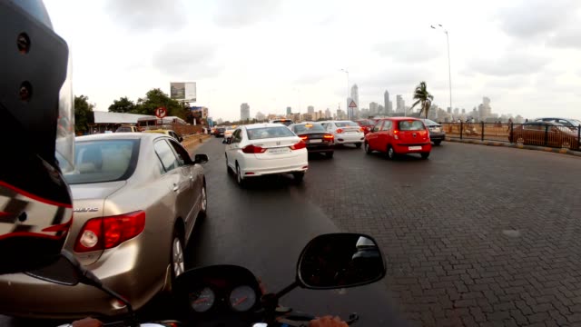 POV-motorcyclist-slips-through-traffic-on-road-near-sea-far-skyscrapers-Mumbai