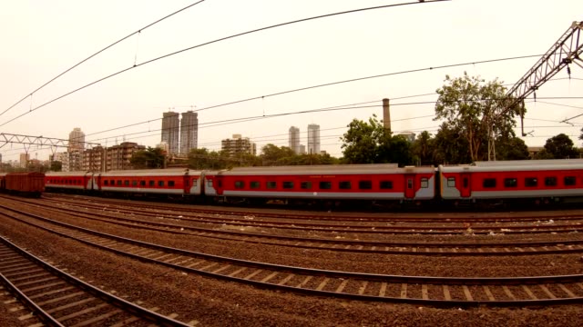 Nahverkehrszüge-bleiben-Zug-mit-roten-Vagonen-weit-Wolkenkratzer-und-grüne-Bäume-Mumbai