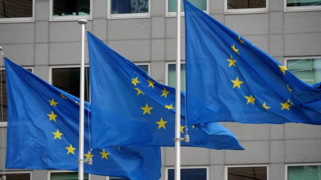 Emocionante-vista-de-tres-banderas-de-la-Unión-Europea-con-círculos-de-estrellas-amarillas-que-ondean-en-el-edificio-de-la-UE-en-Bruselas-en-un-día-soleado-en-primavera.