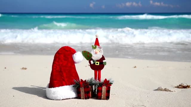 Christmas-Helper-Hat,-Santa-Claus-toy-and-present-box-on-caribbean-beach