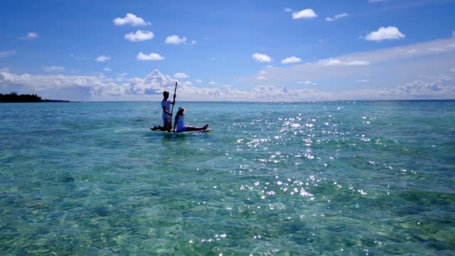 v03860-vuelo-drone-vista-aérea-de-Maldivas-playa-2-personas-pareja-hombre-mujer-relajante-en-paddleboard-en-isla-paraíso-soleado-con-cielo-azul-aqua-agua-mar-4k