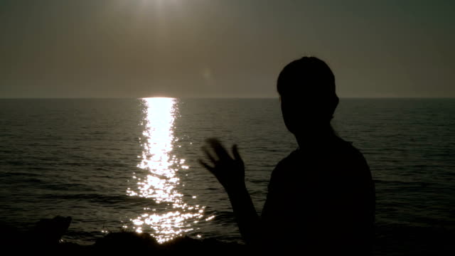 Ein-Mädchen,-schwenkten-ihre-Hand-am-Strand-bei-Sonnenuntergang.