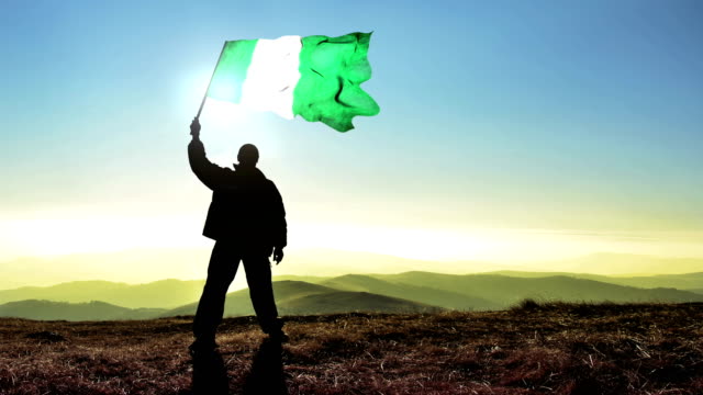 Successful-silhouette-man-winner-waving-Nigeria-flag-on-top-of-the-mountain-peak,-Cinemagraph-LOOP-background