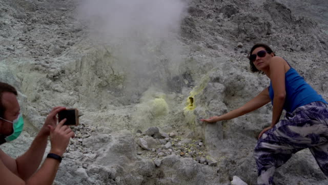 A-man-is-taking-pictures-of-a-woman-next-to-a-fumarole-on-a-smartphone