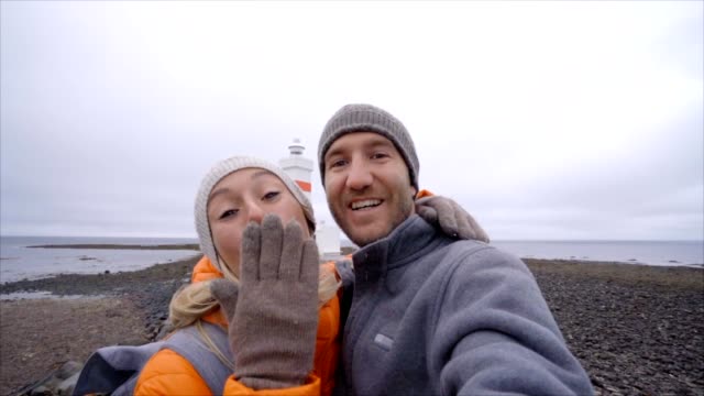 Travel-couple-taking-selfie-at-lighthouse,-girl-blowing-a-kiss