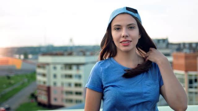 Portrait-of-attractive-smiling-young-teenager-woman-in-cap-touching-her-hair-outdoor