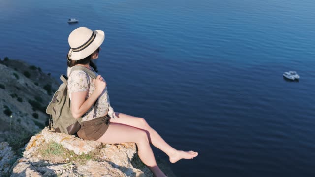 High-angle-playful-backpack-barefoot-woman-in-hat-enjoying-view-of-bay-and-seascape