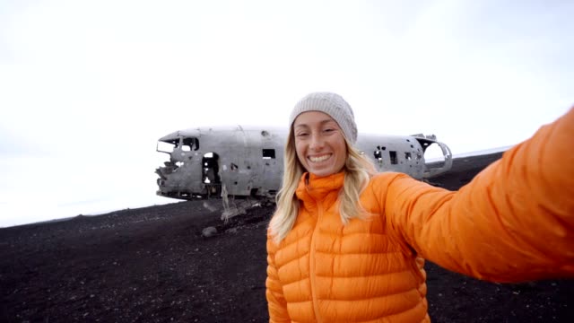 4K-joven-por-ruina-del-aeroplano-en-la-playa-de-arena-negra,-produciendo-una-selfie-retrato-famoso-para-visitar-en-Islandia-y-posan-junto-a-los-restos-del-naufragio
