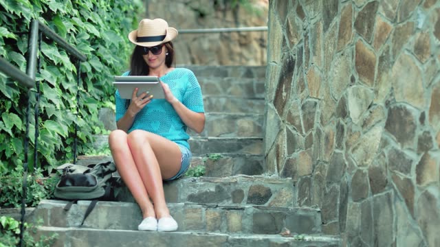 Tiro-completo-bonita-a-mujer-turista-relajada-sentado-en-las-escaleras-con-escalones-de-piedra-con-tablet-PC