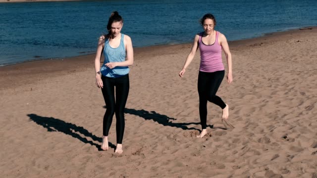 Dos-mujeres-haciendo-estiramientos-después-de-correr-a-lo-largo-de-la-playa-de-arena-de-río-al-atardecer.