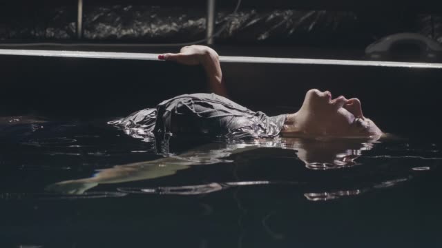 Mujer-joven-en-agua-superficial-suave-en-piscina-sobre-fondo-oscuro