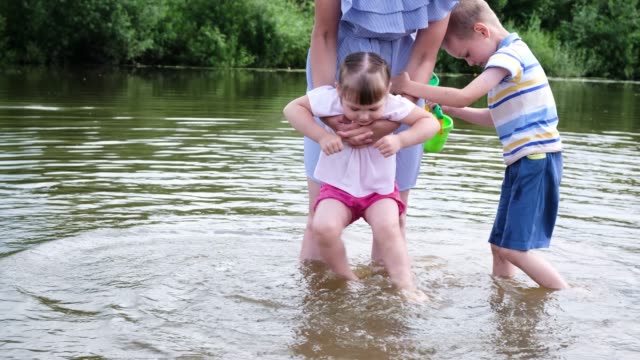 Mutter-des-kleinen-Mädchens-wäscht-seine-Füße-im-Fluss.-Eine-Frau-steht-im-Wasser-mit-ihren-Kindern
