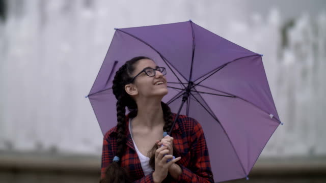 Mädchen-mit-Regenschirm-im-Park-auf-dem-Hintergrund-eines-Brunnens,-schaut-in-die-Kamera