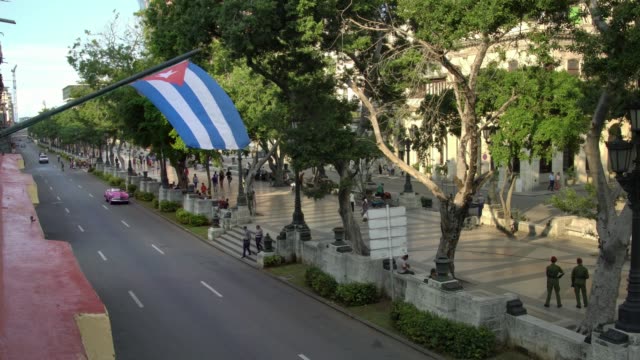 high-angle-establishing-shot-of-classic-convertible-car-on-street-with-cuban-flag-in-Havana,-Cuba