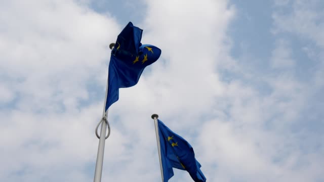Wunderbarer-Blick-auf-zwei-FLAGGEN-der-Europäischen-Union,-die-an-einem-sonnigen-Frühlingstag-am-EU-Hauptsitz-in-Brüssel-wehen.-Der-Himmel-ist-celeste-und-weiß.