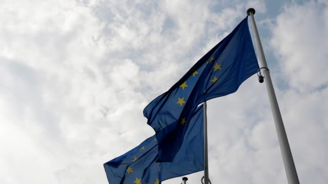 Espléndida-vista-de-dos-banderas-de-la-Unión-Europea-ondeando-solemnemente-en-Bruselas-en-un-día-soleado-en-primavera-en-slo-mo-El-cielo-es-azul-y-blanco