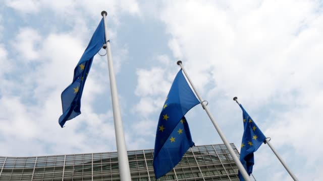Beeindruckende-Aussicht-auf-drei-Flaggen-der-Europäischen-Union,-die-an-einem-sonnigen-Frühlingstag-am-EU-Hauptsitz-in-Brüssel-flattern.-Der-Himmel-ist-blau-und-weiß.