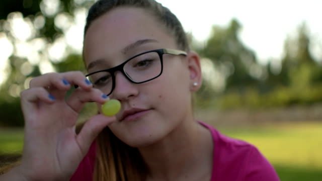Cheerful-teenage-girl-showing-and-eating-grapes-in-front-of-camera
