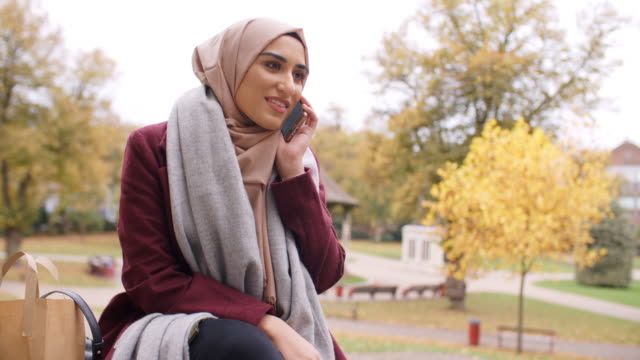 Mujer-musulmana-británica-usando-el-teléfono-móvil-en-el-parque-de-vacaciones