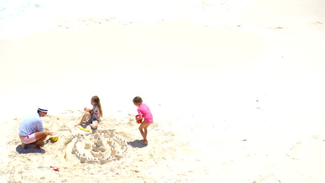 Vista-desde-arriba-a-padre-e-hijas-poco-haciendo-castillos-de-arena-en-la-playa-tropical