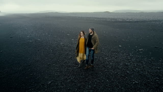 Luftaufnahme-des-Ehepaars-junge-Hipster-zu-Fuß-auf-schwarzen-Vulkanstrand-in-Island.-Mann-und-Frau,-die-die-Natur-genießen