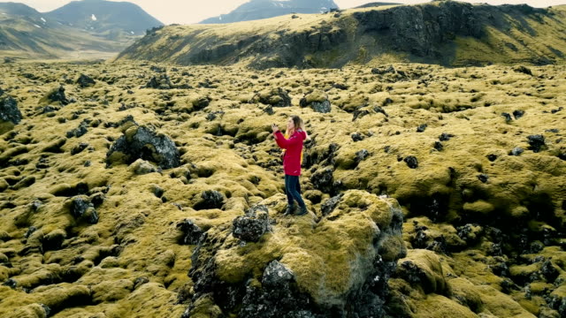 Vista-aérea-de-dos-mujer-feliz-de-pie-en-el-campo-de-lava-en-Islandia-y-haciendo-foto-selfie-en-smartphone