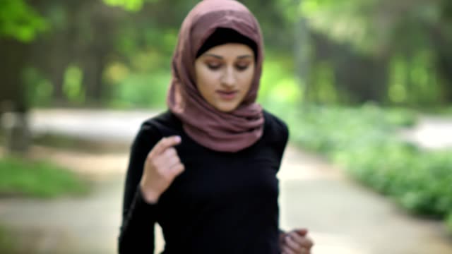 Portrait-of-a-young-girl-running-in-a-frame-in-hijab,-on-nature,-in-a-park-in-the-background.-50-fps