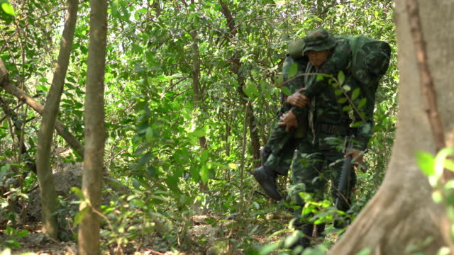 Soldier-holding-gun-weapon-and-waring-armor-uniform-with-smoke.-Soldiers-are-taking-the-wounded-man-out-of-the-jungle.