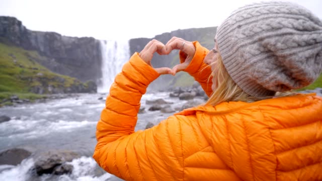 Mujer-joven-en-Islandia-que-marco-del-dedo-corazón-forma-en-espectacular-cascada