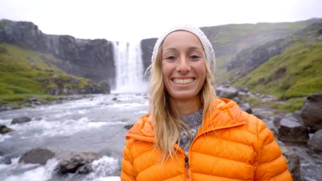 Portrait-of-blond-hair-woman-front-of-magnificent-waterfall-in-Iceland