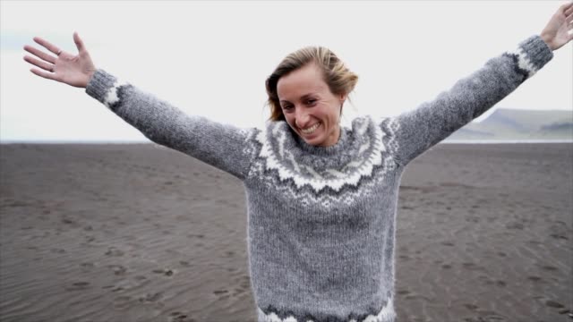 Young-woman-arms-outstretched-by-the-sea-standing-on-black-sand-beach,-hair-in-wind--Iceland---Female-running-playful-enjoying-nature-and-freedom--Slow-motion