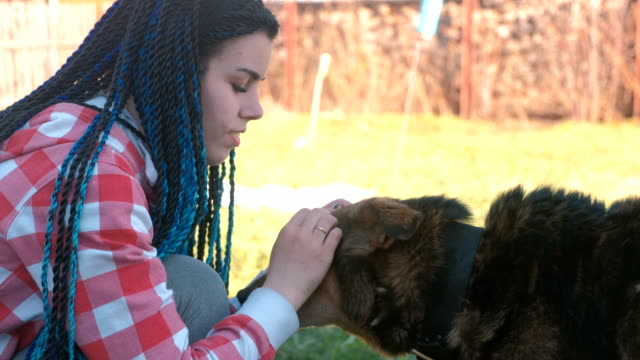 Young-woman-with-blue-braids-hairs-pet-the-dog-outside.