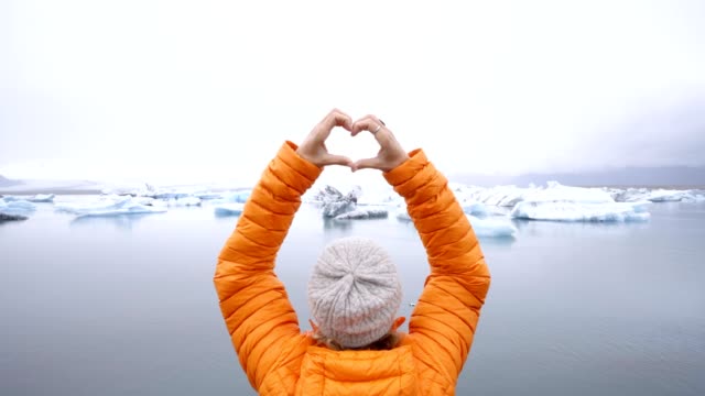 Young-woman-making-heart-shape-finger-frame-on-glacier-lagoon-in-Iceland