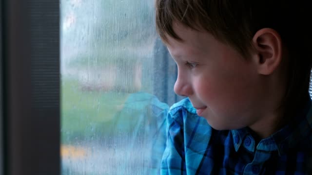 Boy-looks-out-the-window-in-the-rain-and-is-sad.