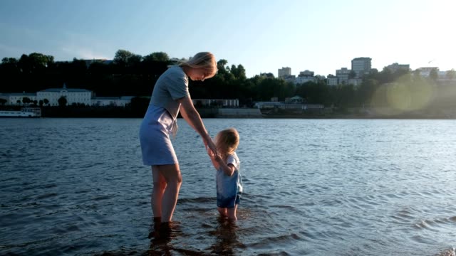 Mamá-y-niña-jugando-en-la-playa-del-río-en-la-puesta-de-sol-y-nadar.