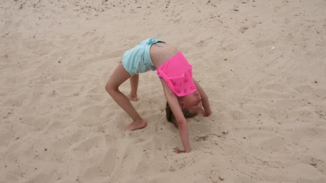 Young-acrobatic-girl-doing-gymnastic-bridge-and-somersaults-on-sand