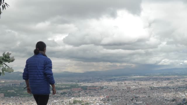 Frau-zu-Fuß-in-Richtung-und-mit-Blick-auf-die-Stadt-von-Bogota-aus-den-Bergen,-in-Zeitlupe