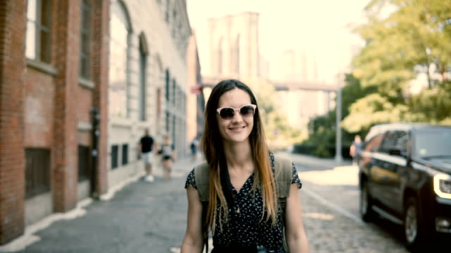 Camera-follows-happy-excited-European-tourist-girl-with-backpack-and-camera-in-sunglasses-smiling,-turning-around-4K