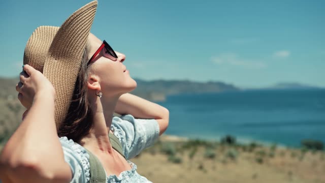 Side-view-relaxing-European-woman-taking-sunbathing-touching-hat-by-hands-and-raising-arms