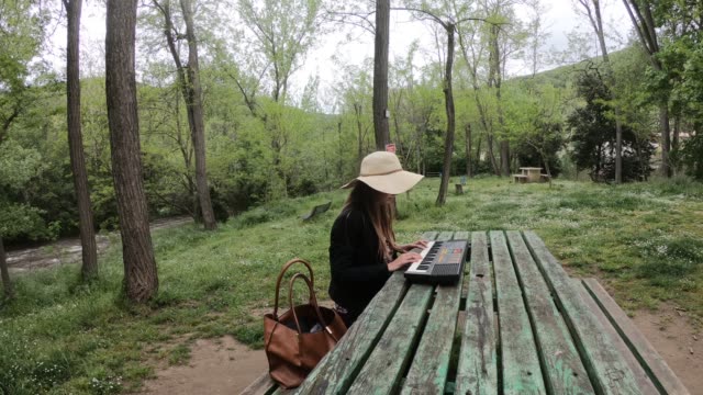 junge-und-schöne-Frau-spielen-Synthesizer-auf-dem-Tisch-eines-Parks,-Frankreich