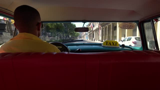 Taxi-driver-in-classic-American-1950's-vintage-car-drive-on-famous-street-in-old-Havana-neighborhood,-Cuba