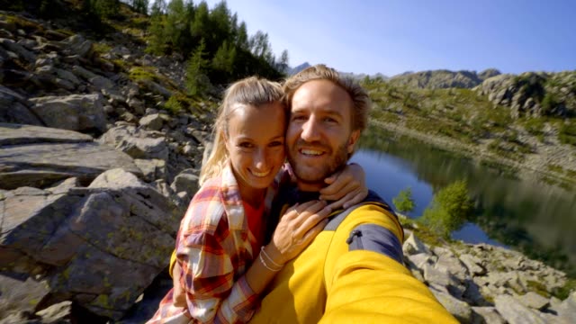 Young-couple-hiking-in-summer-in-the-Swiss-Alps-take-selfie-portrait-by-mountain-lake.-Hikers,-couple--taking-selfie-portrait-on-mountain-trail