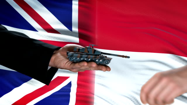 Great-Britain-and-Indonesia-officials-exchanging-tank-for-money,-flag-background