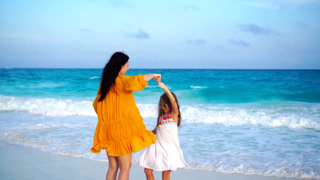Little-adorable-girl-and-young-mother-at-tropical-beach-in-warm-evening-with-beautiful-sunset