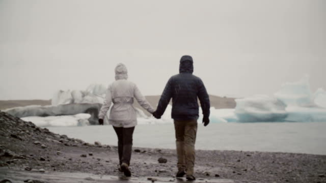 Rückansicht-des-jungen-Paares-gehen-in-Eis-Lagune-in-Island.-Mann-und-Frau-die-Eisberge-und-Gletscher-erkunden